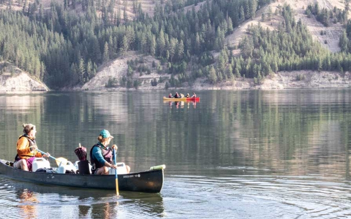 two girls paddle a canoe on still water. there is another canoe in the background